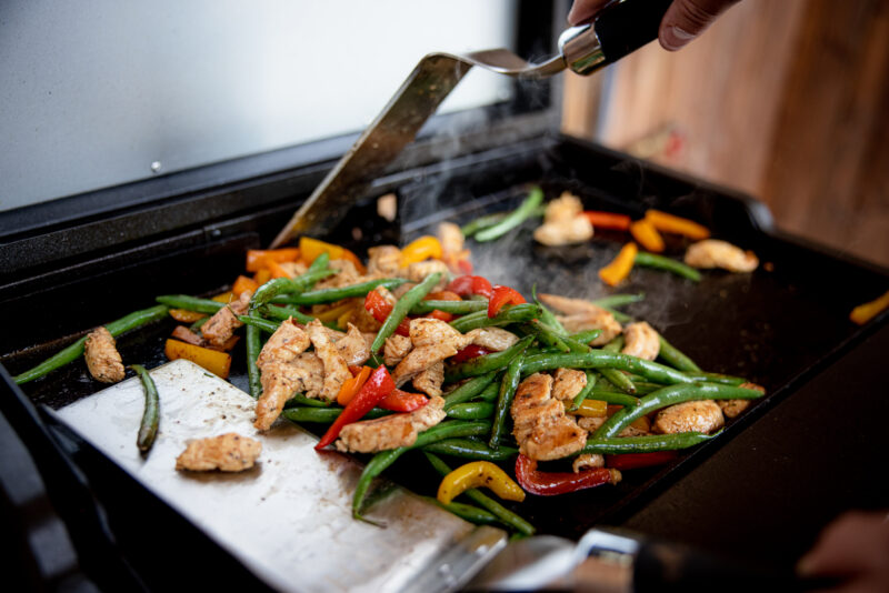 Person cooking chicken and vegetables on the Elite1B countertop outdoor griddle
