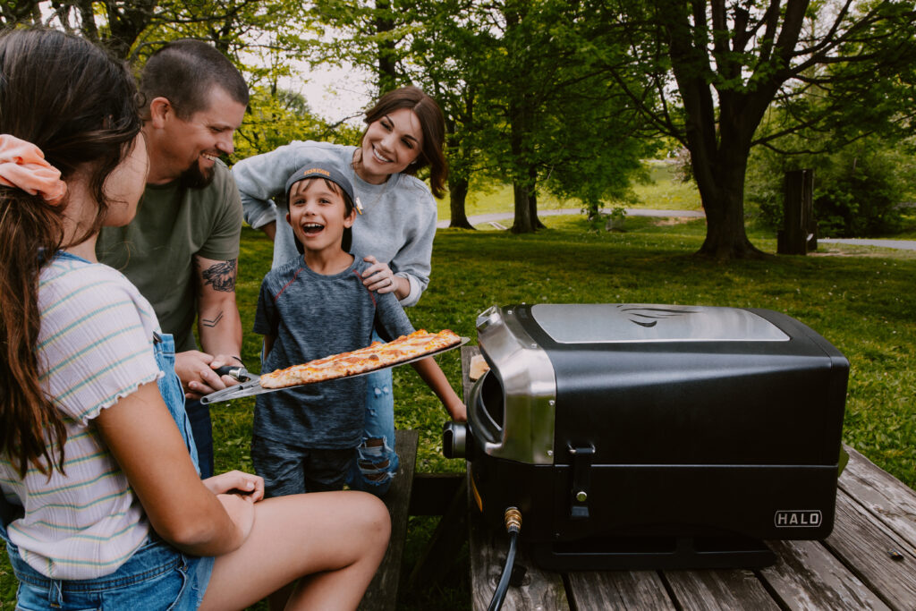 A family making homemade pizza in a portable pizza oven.