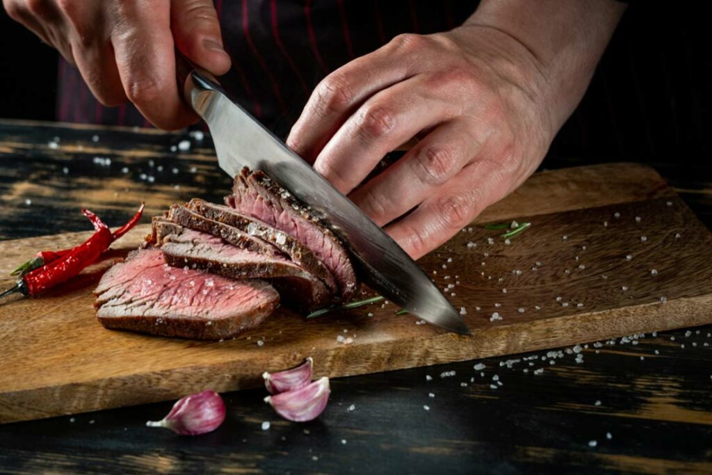 Cooking juicy beef steak by chef hands on dark black background