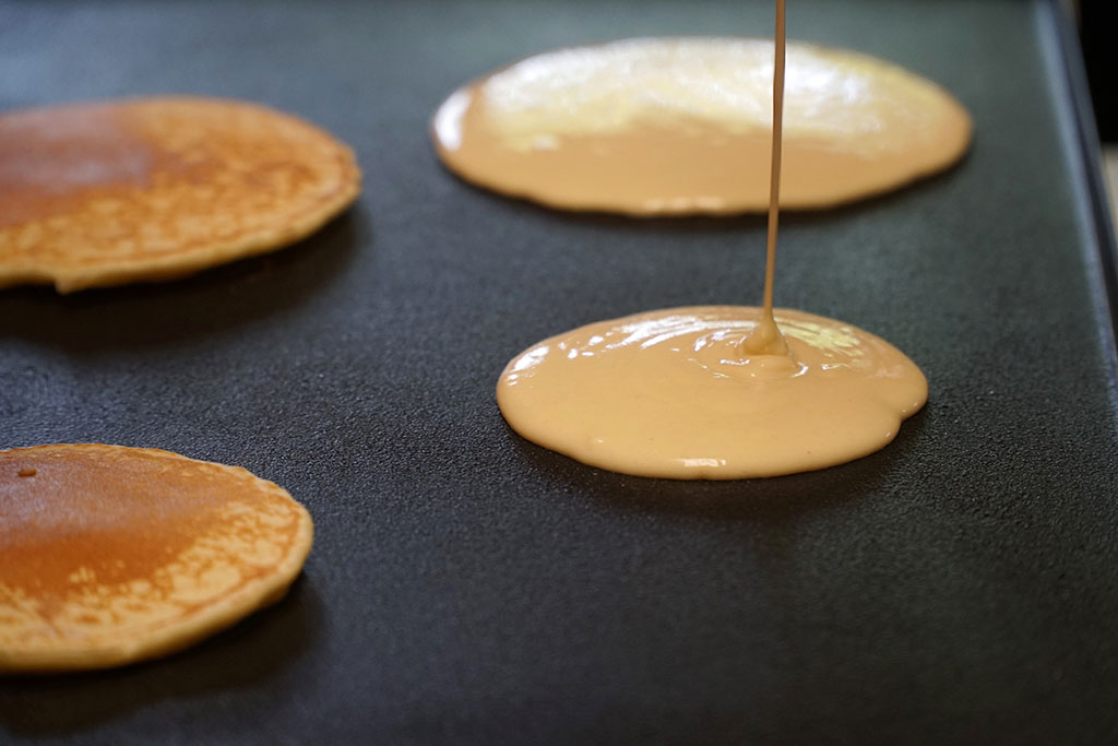 Pancake batter baking mix being poured from a bowl onto a hot griddle.